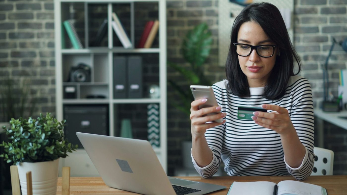 Mulher à mesa olhando o celular para aumentar limite pelo aplicativo do banco