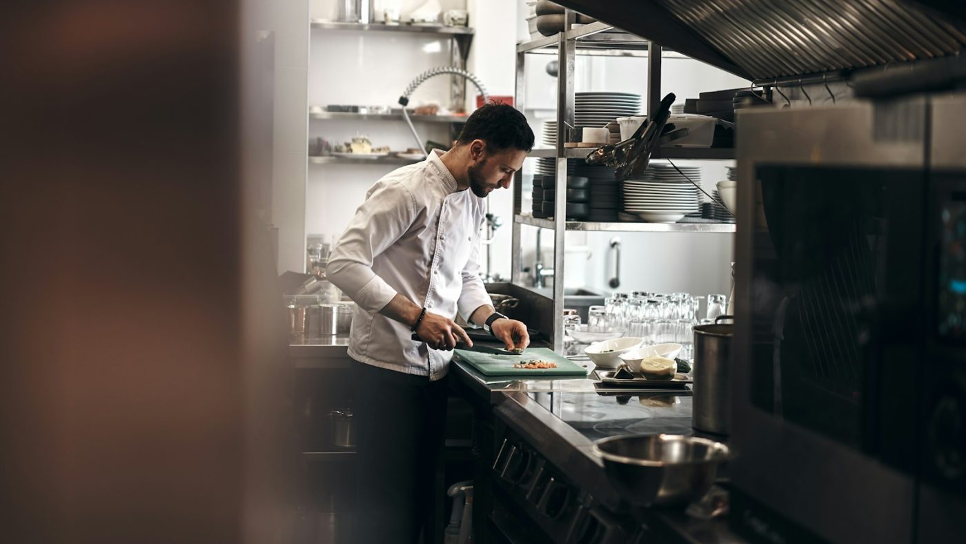 Auxiliar de cozinha de dólmã branca cortando legumes na tábua