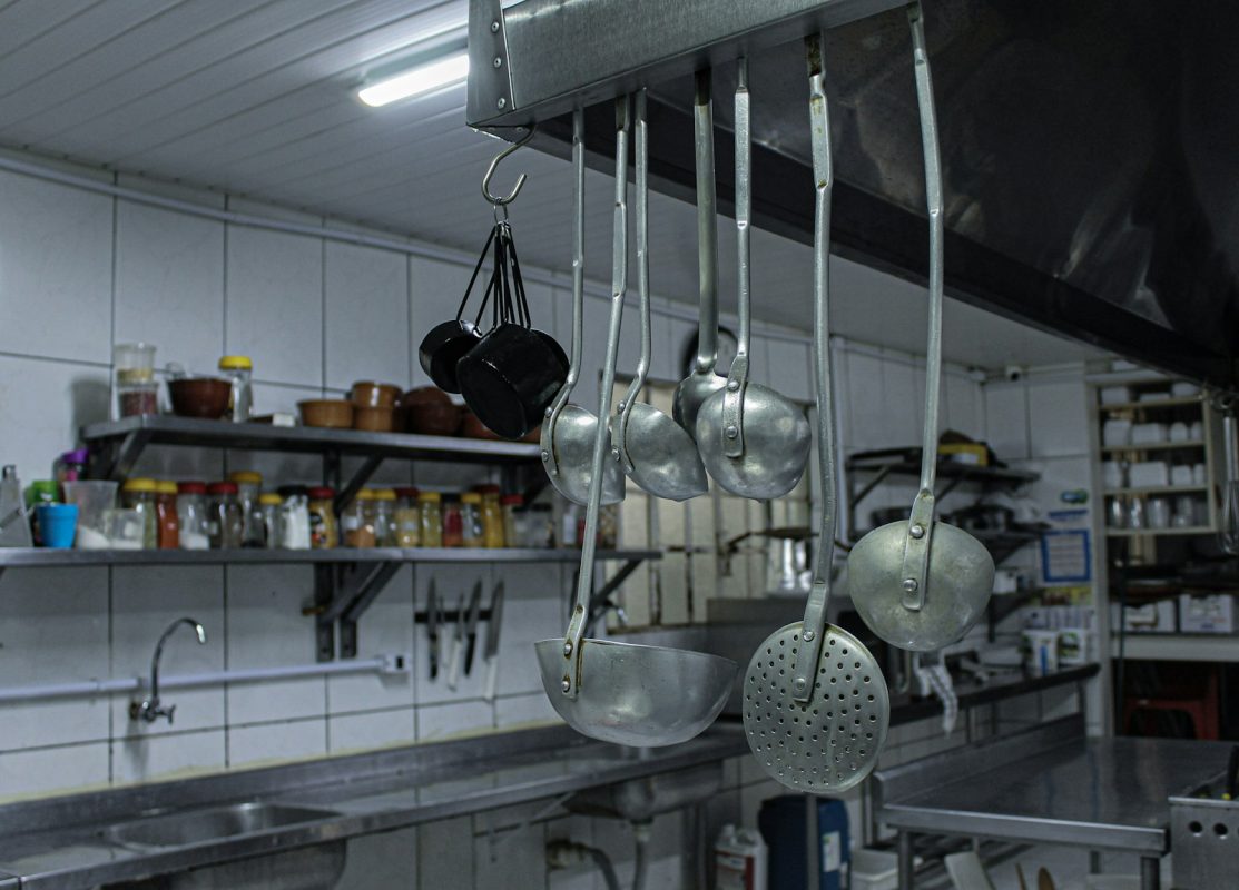 Auxiliar de cozinha organiza panelas e utensílios em cozinha industrial