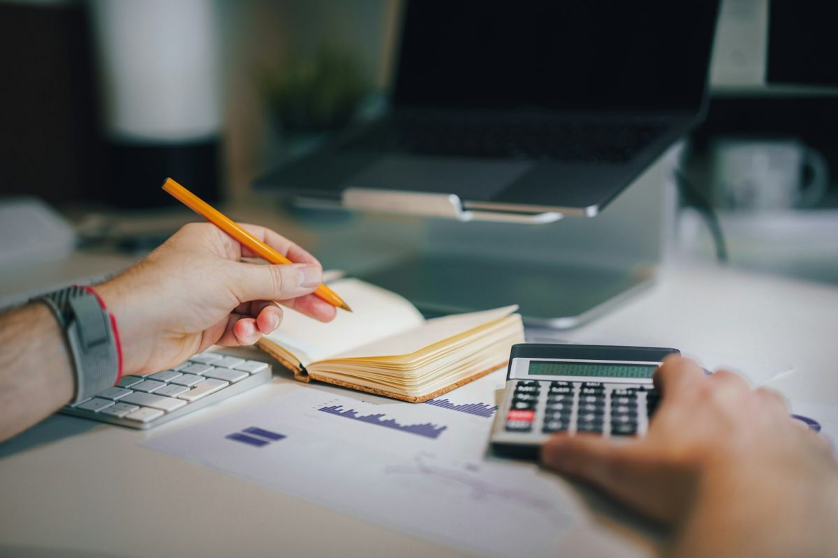 Pessoa à mesa com calculadora e caderno fazendo o controle financeiro da renda variável