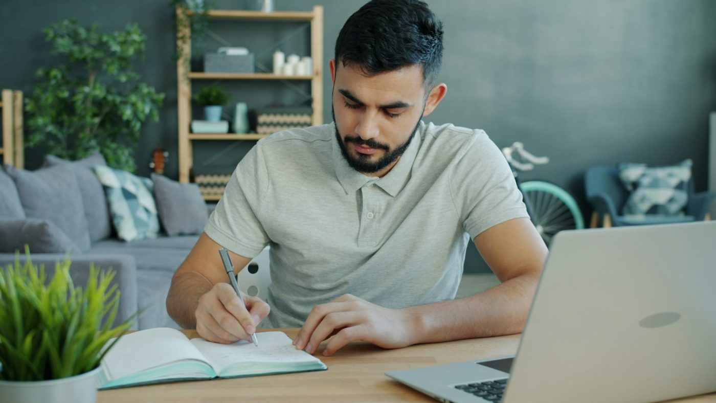 Estudante fazendo anotações com laptop para a prova do estágio Banrisul