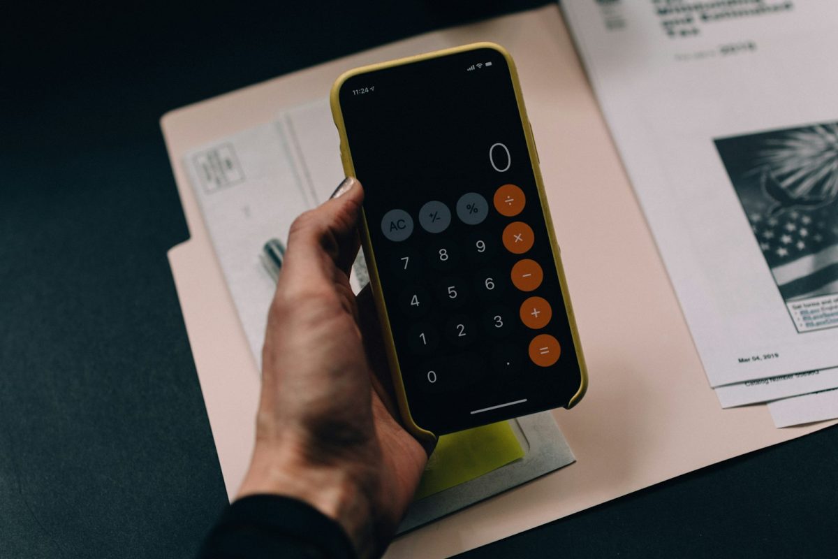 Saque-aniversário do FGTS: mão segurando celular com calculadora aberta sobre documentos
