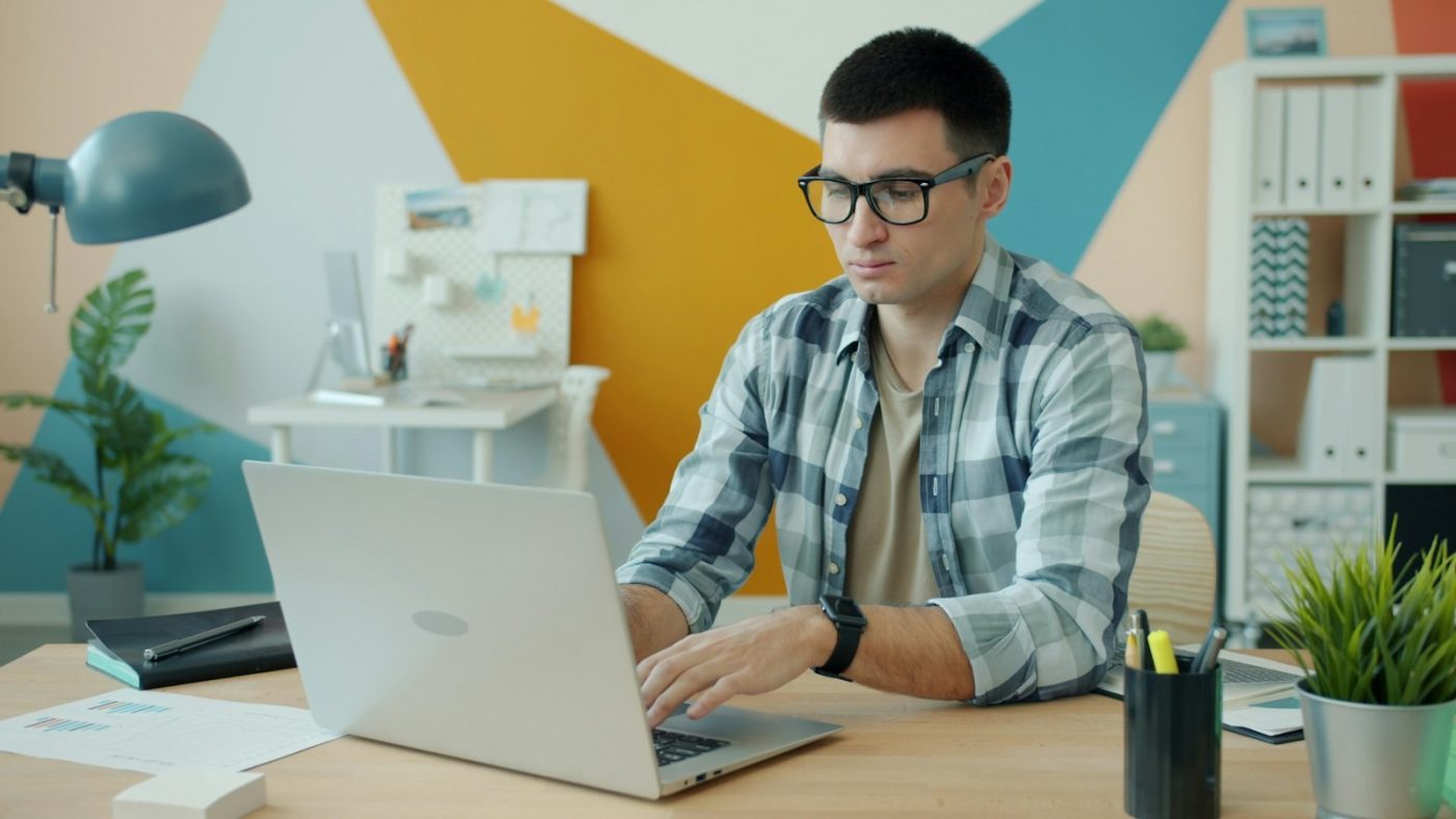 Homem de óculos digitando no laptop para completar o currículo na Gupy