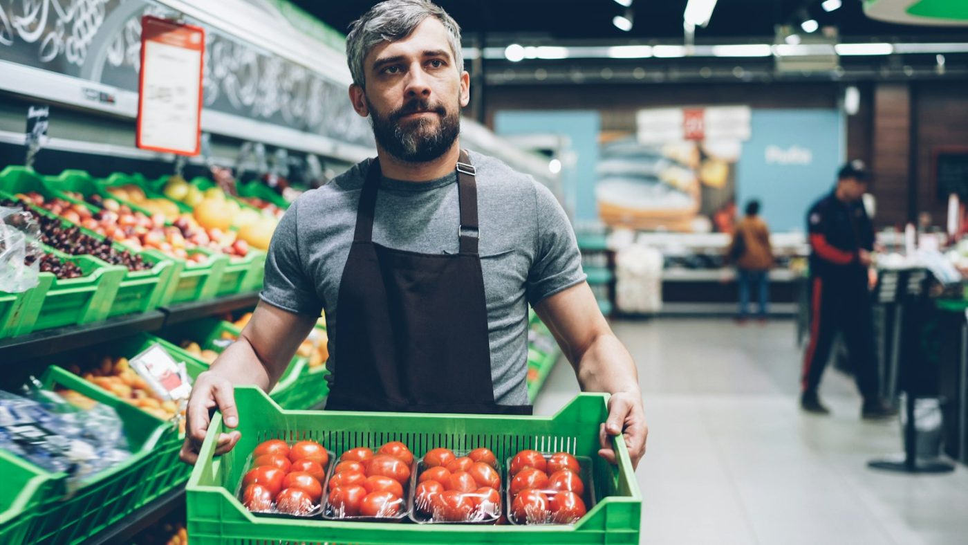 Funcionário de supermercado com caixa de tomates, setor entre as melhores vagas de emprego para iniciantes